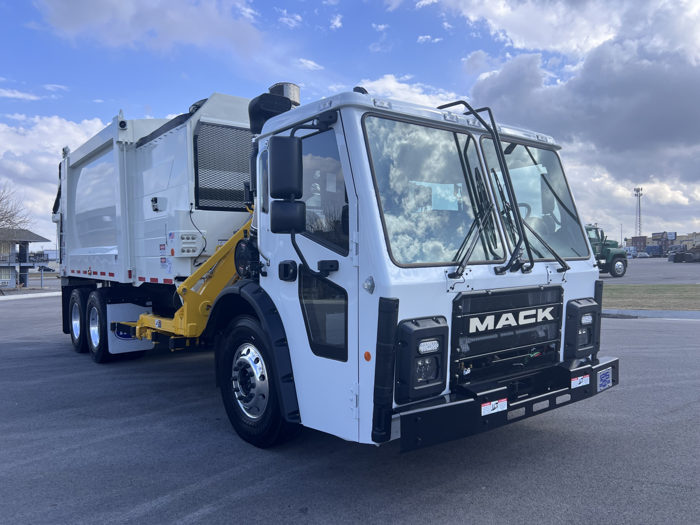 Mack LR64 heavy-duty cab forward truck with a white cab and a rear garbage body visible, front grille with MACK badge, large side mirrors, photographed in a lot.