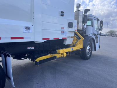 Scrubber truck rear view showing the yellow hitch/ramps and lower rear chassis attached to a white Mack LR64 cab, side of cargo body visible with reflective tape.