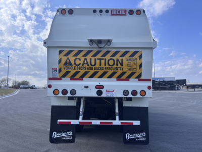 Rear view of a white Mack LR64 dump truck showing caution sign, taillights, mud flaps with Bruckner’s logo, and rear bumper; VIN and stock number not visible in text.