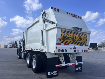 Rear view of a white Mack LR64 dump truck showing cargo box and taillights with caution sign and license plate area.