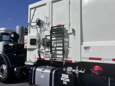 Truck rear showing hydraulics and ladder rack on a 2026 Mack LR64 dump truck with white body and black components.
