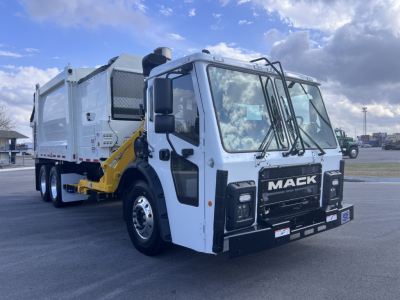Mack LR64 heavy-duty cab forward truck with a white cab and a rear garbage body visible, front grille with MACK badge, large side mirrors, photographed in a lot.