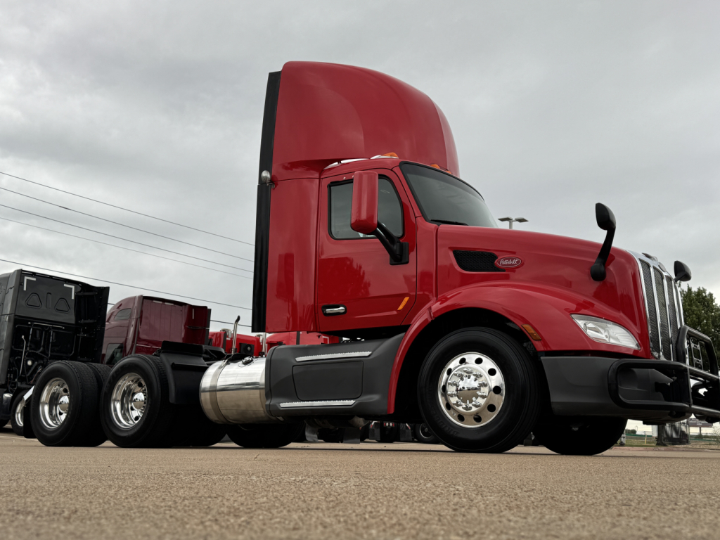 Peterbilt 579 conventional daycab truck in red with sleeper and cargo bed showing side view and front grille.