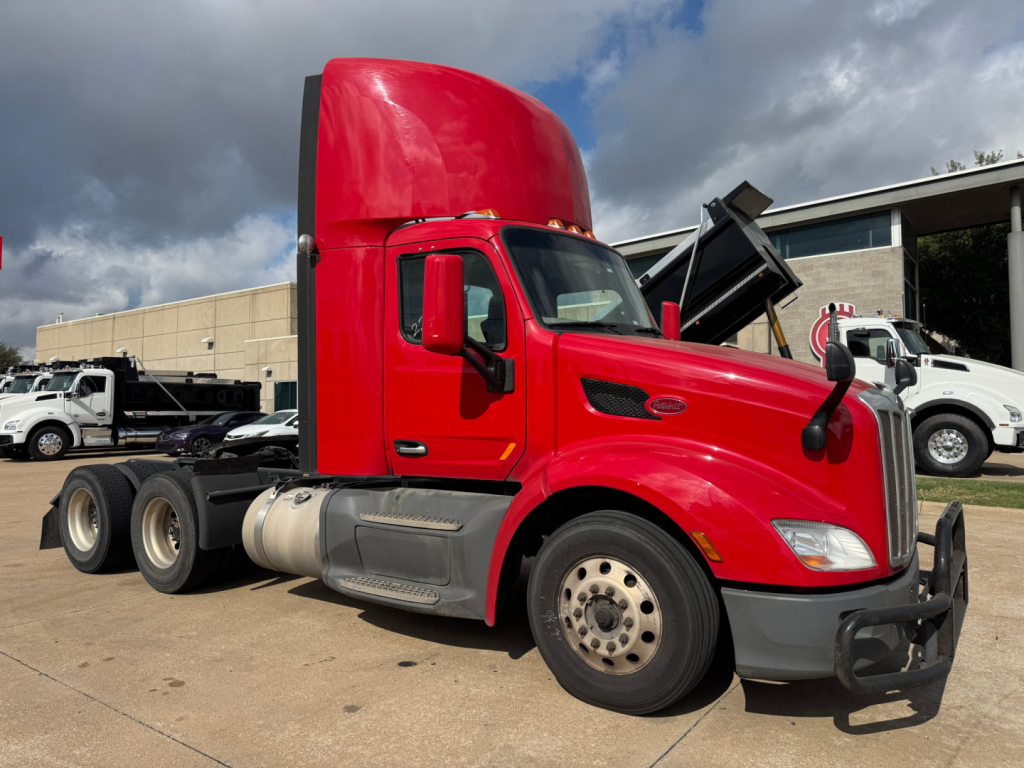 Peterbilt 579 truck in red with raised hood on a lot, side view showing cab, wheels, and chassis; no visible text on the image aside from vehicle features.