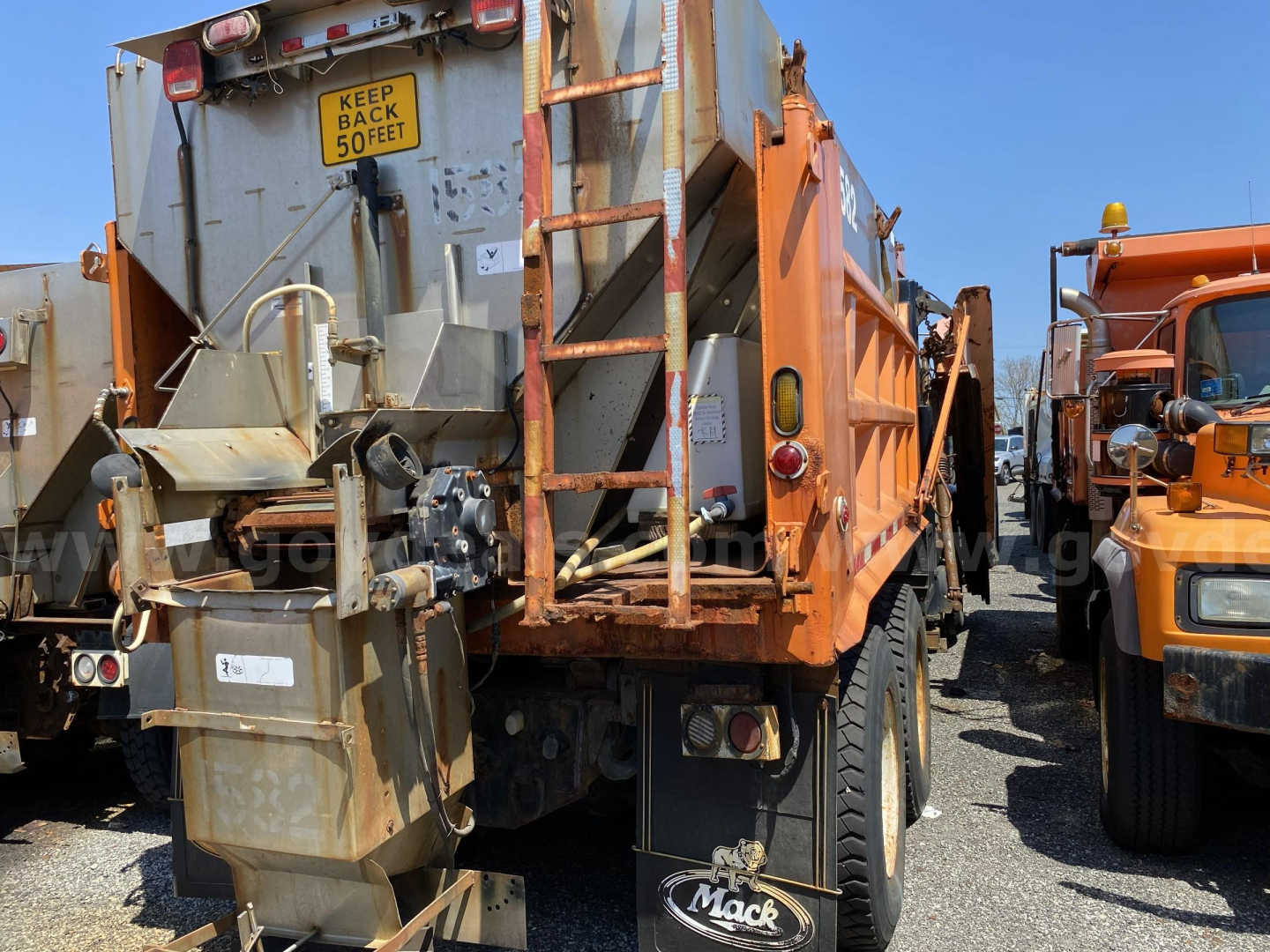 Mack CV713 dump truck rear view showing warning sign 'KEEP BACK 50 FEET' and load body with hydraulic system.