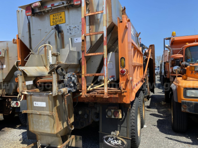 Mack CV713 dump truck rear view showing warning sign 'KEEP BACK 50 FEET' and load body with hydraulic system.