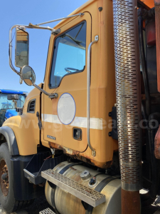 Mack CV713 truck cab showing side view with orange paint and chrome exhaust stack.
