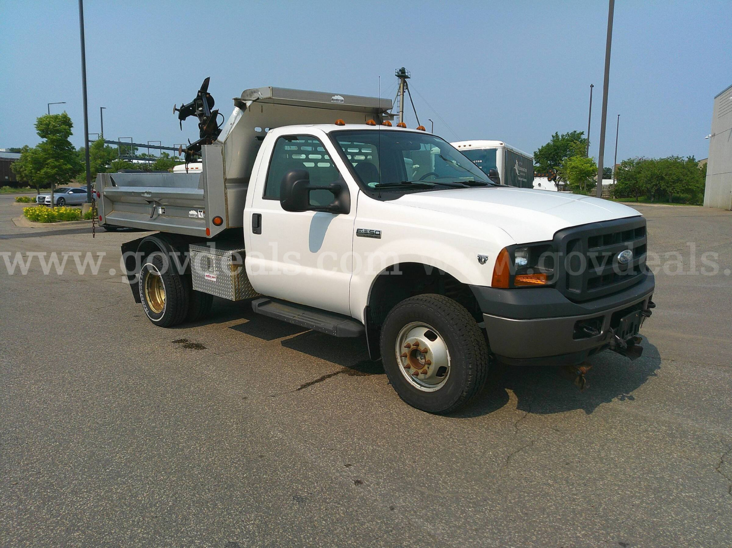 White Ford F-350 dump truck in a parking lot with a stake bed and utility crane equipment on the bed.