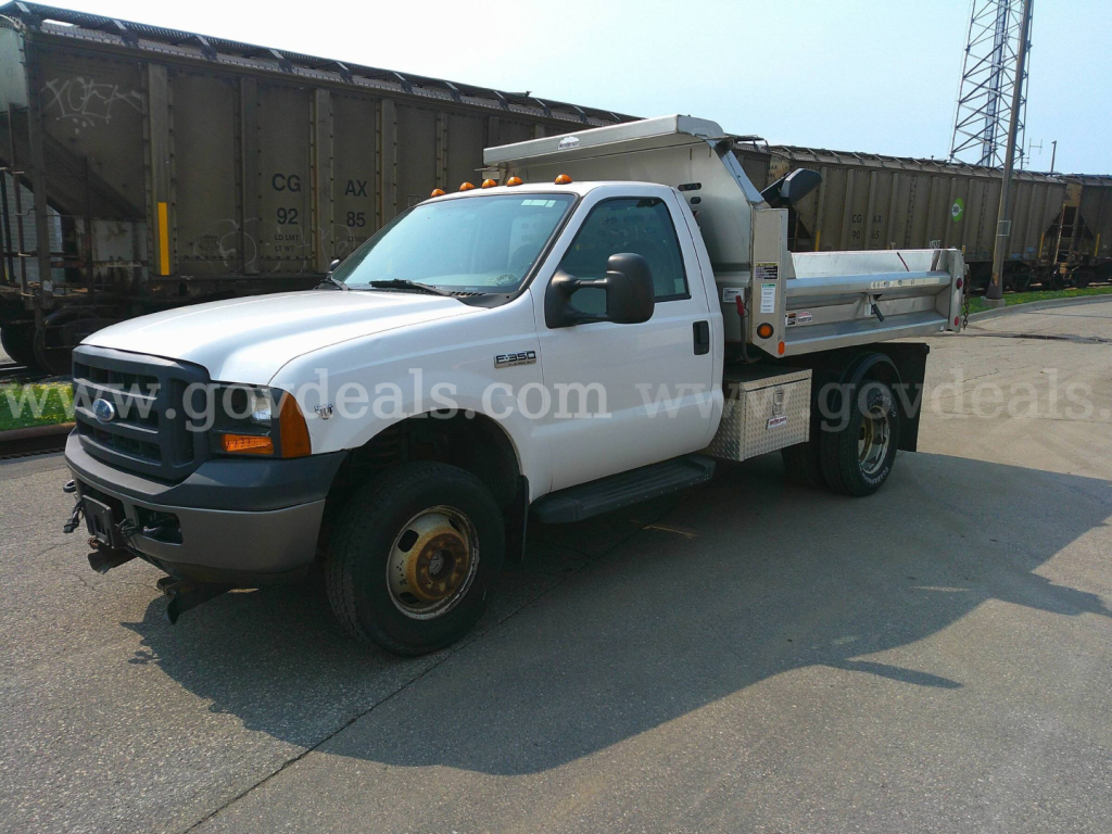 Ford F-350 dump truck in a yard showing cab and dump bed with orange clearance lights and side steps.