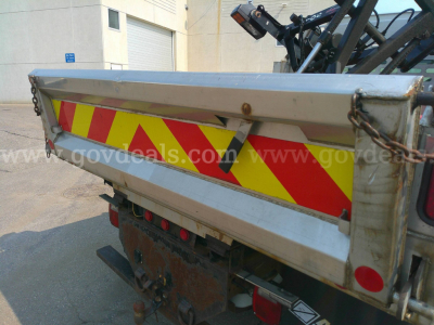 Truck bed side of a 2006 Ford F-350 dump truck showing reflective red-yellow diagonal warning stripes and rear tailgate with chains.