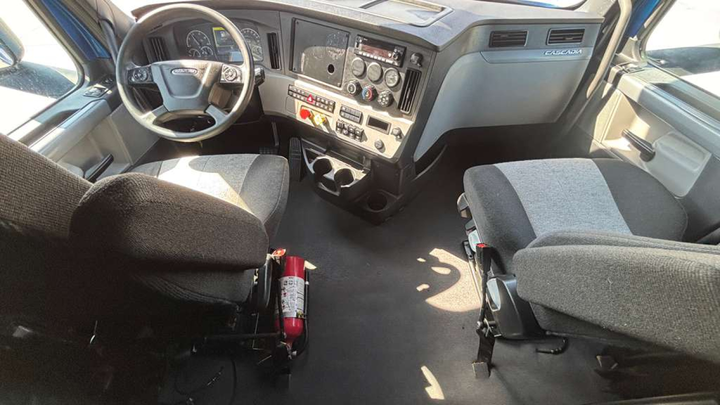 Truck cab interior showing steering wheel, dashboard, and seats with a fire extinguisher mounted near the center console.