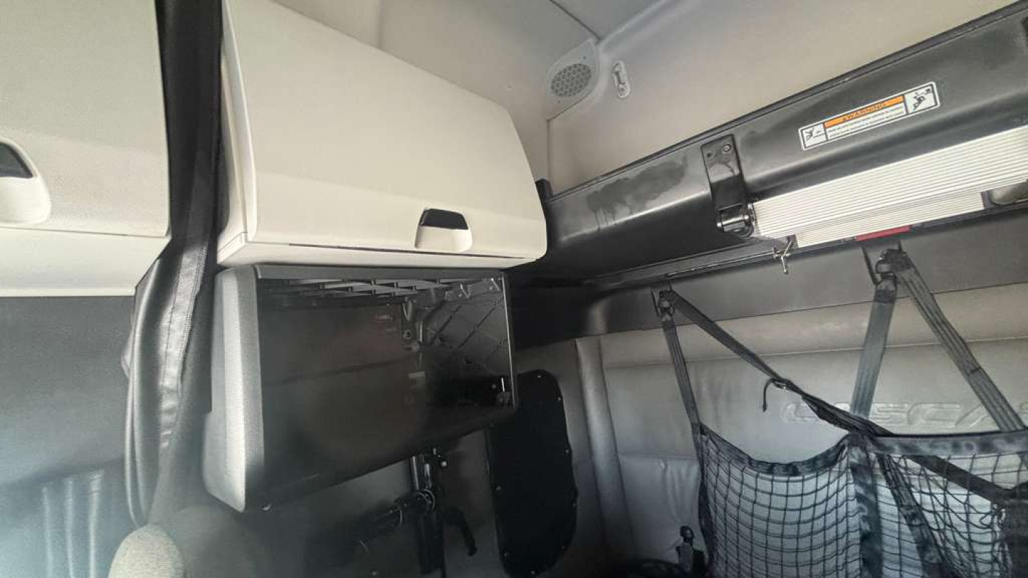 Cab interior of a Freightliner truck showing storage cabinet, overhead shelf, and webbed cargo net. No visible model or part numbers readable.