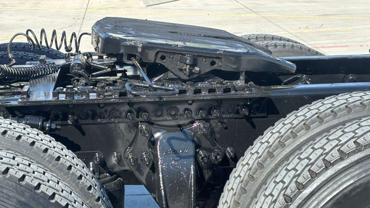Truck chassis with dual rear wheels and suspension components, engine area visible, heavy-duty metal frame and wiring, part of Freightliner sleeper cab.