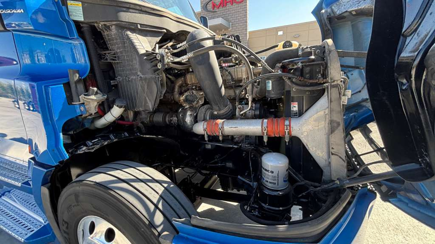 Truck engine bay showing exposed components and intake manifold of a Freightliner PT126064ST with visible hoses, clamps, and a cylindrical filter.