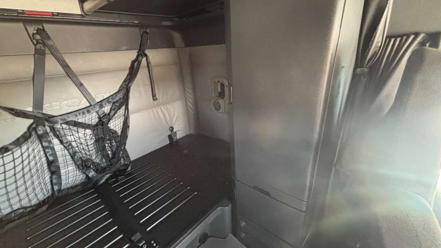 Interior sleeper cab cargo area with netted storage and ribbed floor, side wall panels, and vertical cabinet in a Freightliner truck.