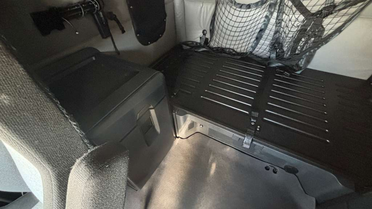 Truck sleeper cab interior with storage and load area; metal bed platform, black panel, netting, and ergonomic compartments visible.