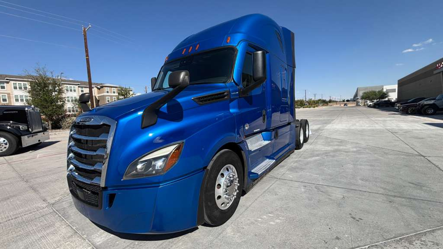 Truck engine bay area not visible; blue 2022 Freightliner PT126064ST conventional sleeper semi truck in a dealership lot with clear sky.