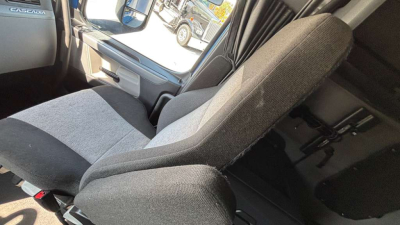 Cabin interior of a Freightliner PT126064ST truck showing grey fabric seats, window, and door panel.
