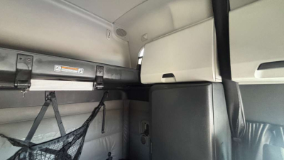 Cab interior of a Freightliner sleeper cab showing overhead storage, strap, and netting with a grey cabinet.