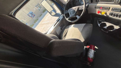 Cab interior of a Freightliner truck showing steering wheel, dashboard with controls, driver seat, and a fire extinguisher mounted near the seat.