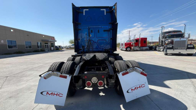 Truck rear view showing fifth-wheel and dual rear axles of a Freightliner tractor with white MHC mud flaps and blue sleeper cab in background.