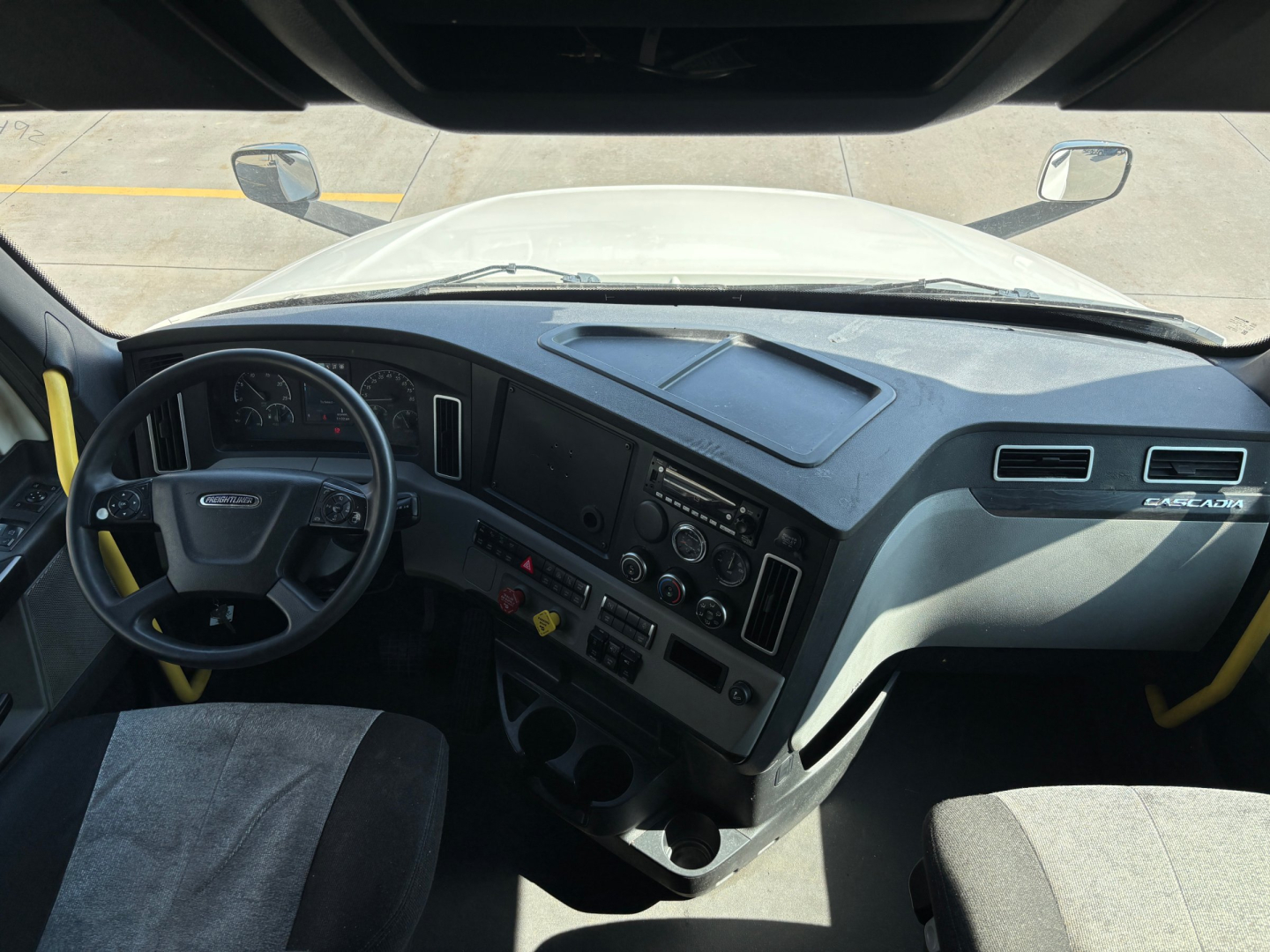 Cab interior of a Freightliner truck with dashboard, steering wheel, and controls visible from the driver's seat in a sleeper tractor.
