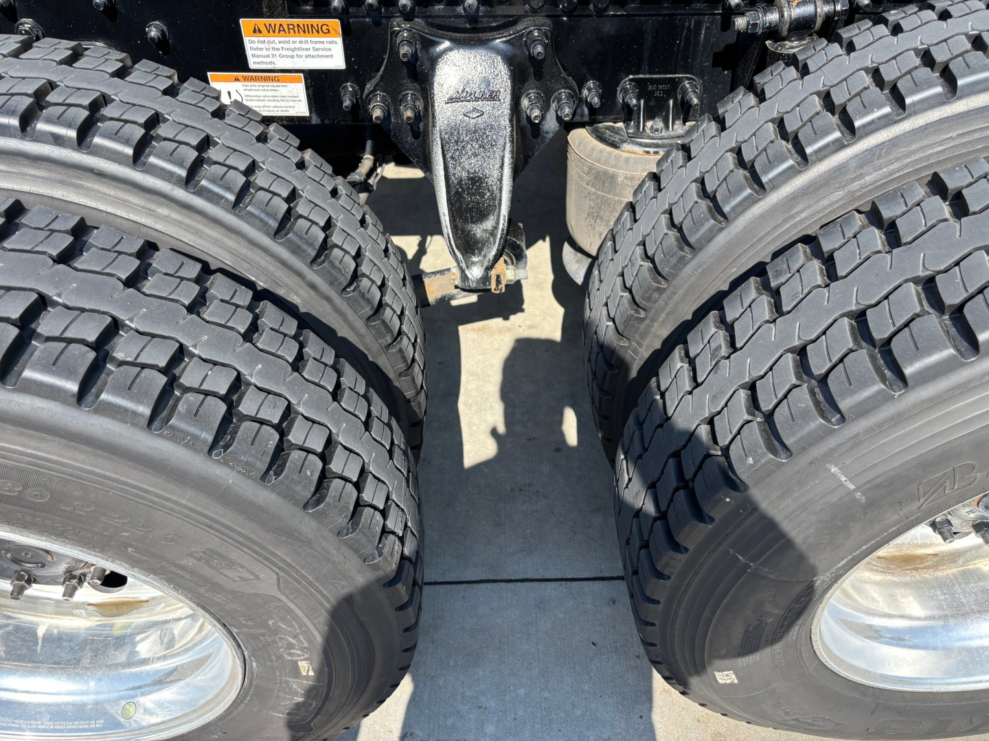 Dual rear axles with heavy-duty truck tires and suspension components visible under a Freightliner truck chassis.