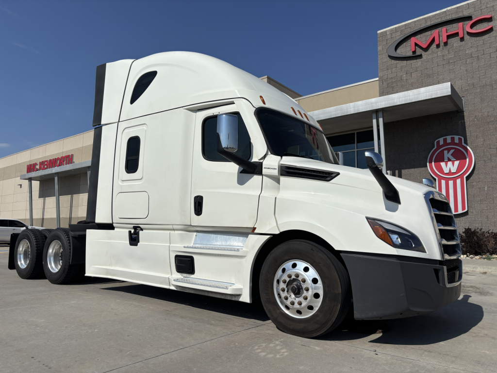 Truck in service bay showing 2023 Freightliner PT126064ST sleeper tractor with white cab and chrome wheels.