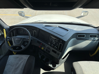 Cab interior of a Freightliner truck with dashboard, steering wheel, and controls visible from the driver's seat in a sleeper tractor.
