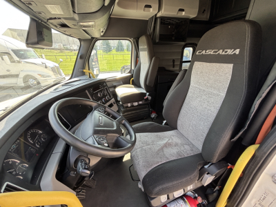 Cab interior of a Freightliner with Casadia driver seat and steering wheel, dashboard, and control panel visible.