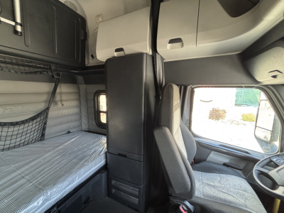 Cab interior of a Freightliner sleeper cab showing driver seat, overhead sleeper bunk area, and storage compartments.