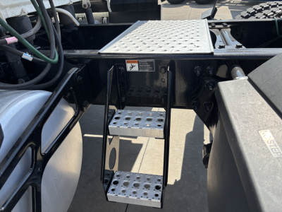 Truck step/entry area of a Freightliner PT126064ST showing aluminum perforated steps, metal platform above, and surrounding chassis components.