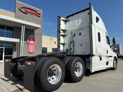 Semi truck chassis and sleeper cab in a lot, rear view showing dual rear axles and components, Freightliner/Conventional Sleeper configuration.