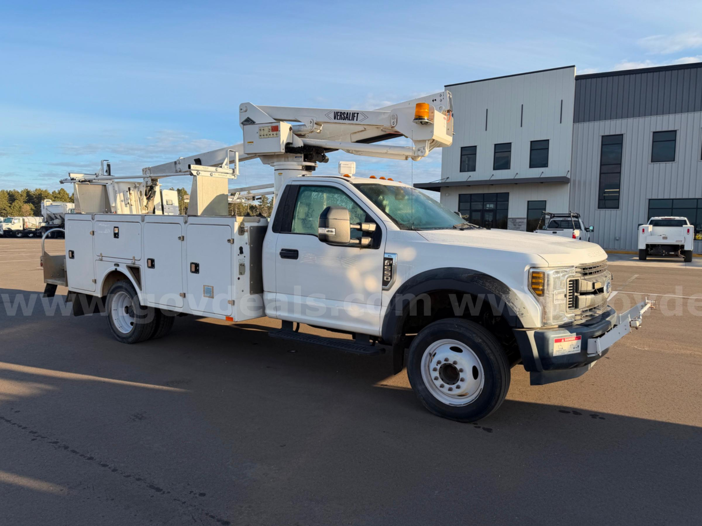 Ford F-550 bucket truck with boom lift on a service lot, side view showing utility compartments and large front grille.