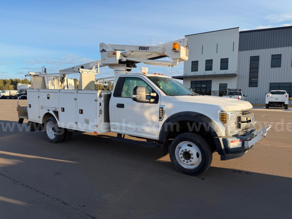 Ford F-550 bucket truck with boom lift on a service lot, side view showing utility compartments and large front grille.