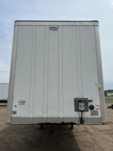 Rear view of a white 2016 Wabash trailer showing riveted walls, rear doors, and bumper with locking mechanism. Visible stickers and license plate area.