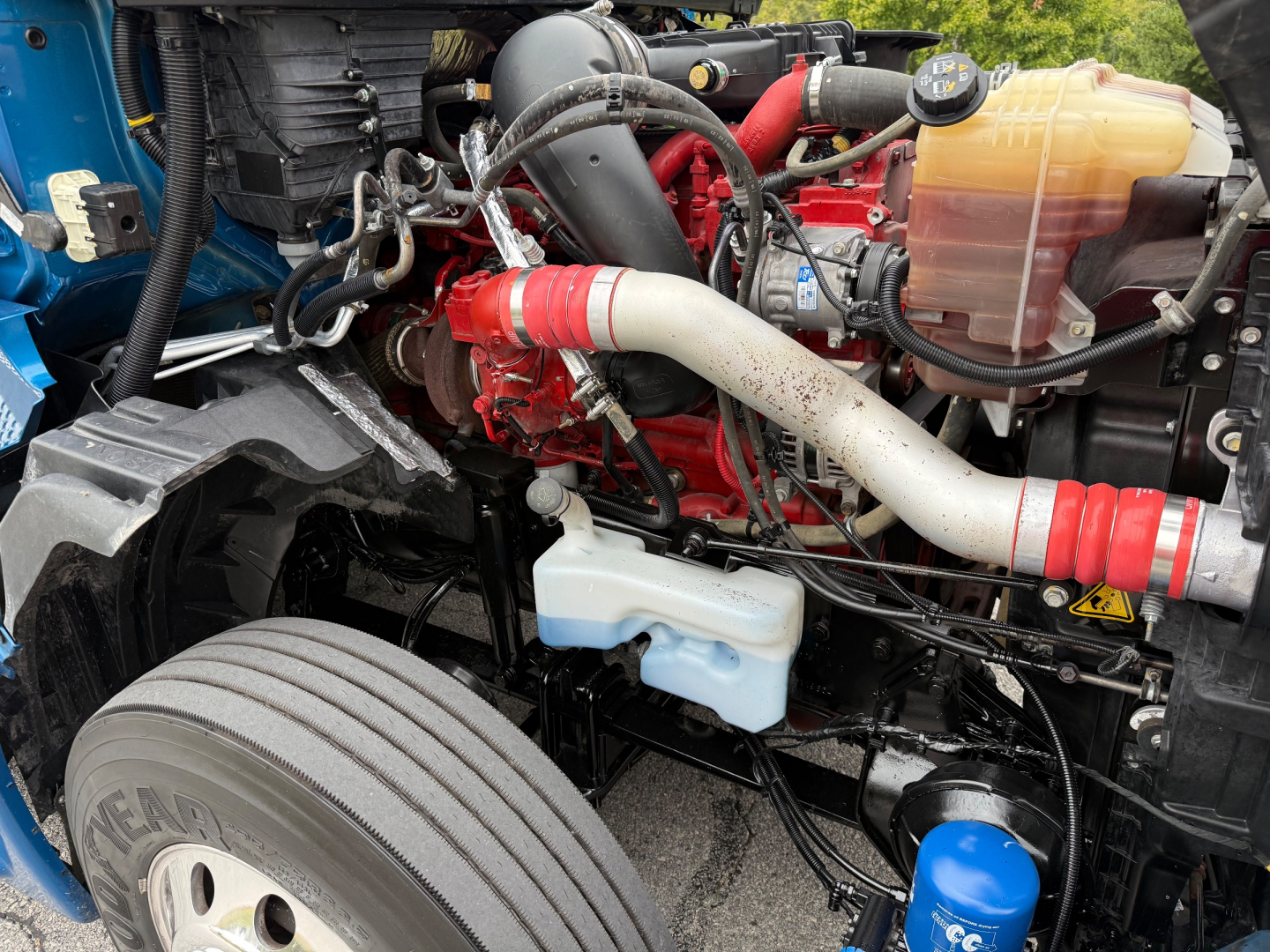 Truck engine bay showing coolant reservoir, blue windshield washer bottle, red engine block, white radiator hose, and yellow/brown translucent coolant reservoir; engine components and hoses visible.