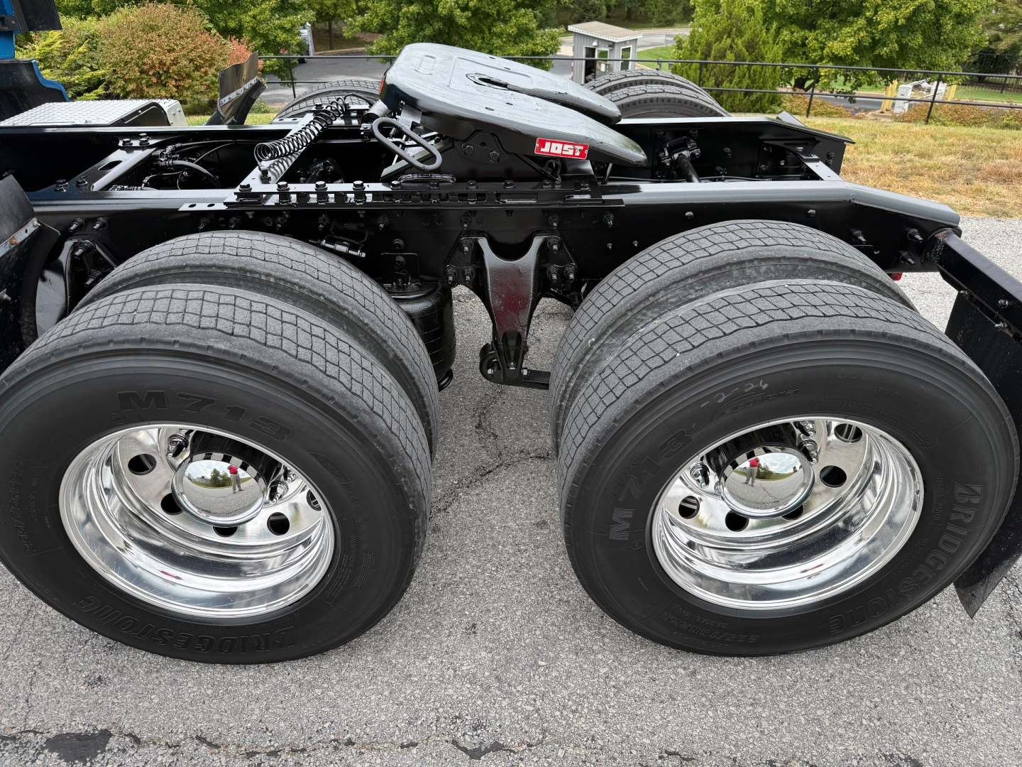 Truck chassis with dual rear axles and large tires. Visible text includes 'M' on tires and chrome wheel hubs; a small red and white label on frame area reads 'JOST'.