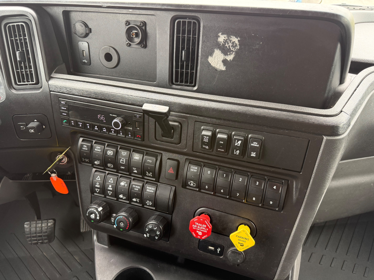 Dashboard and center console of a 2024 International LT625 truck cab showing control switches, gauges, and two colored knobs (red and yellow) under the radio area.