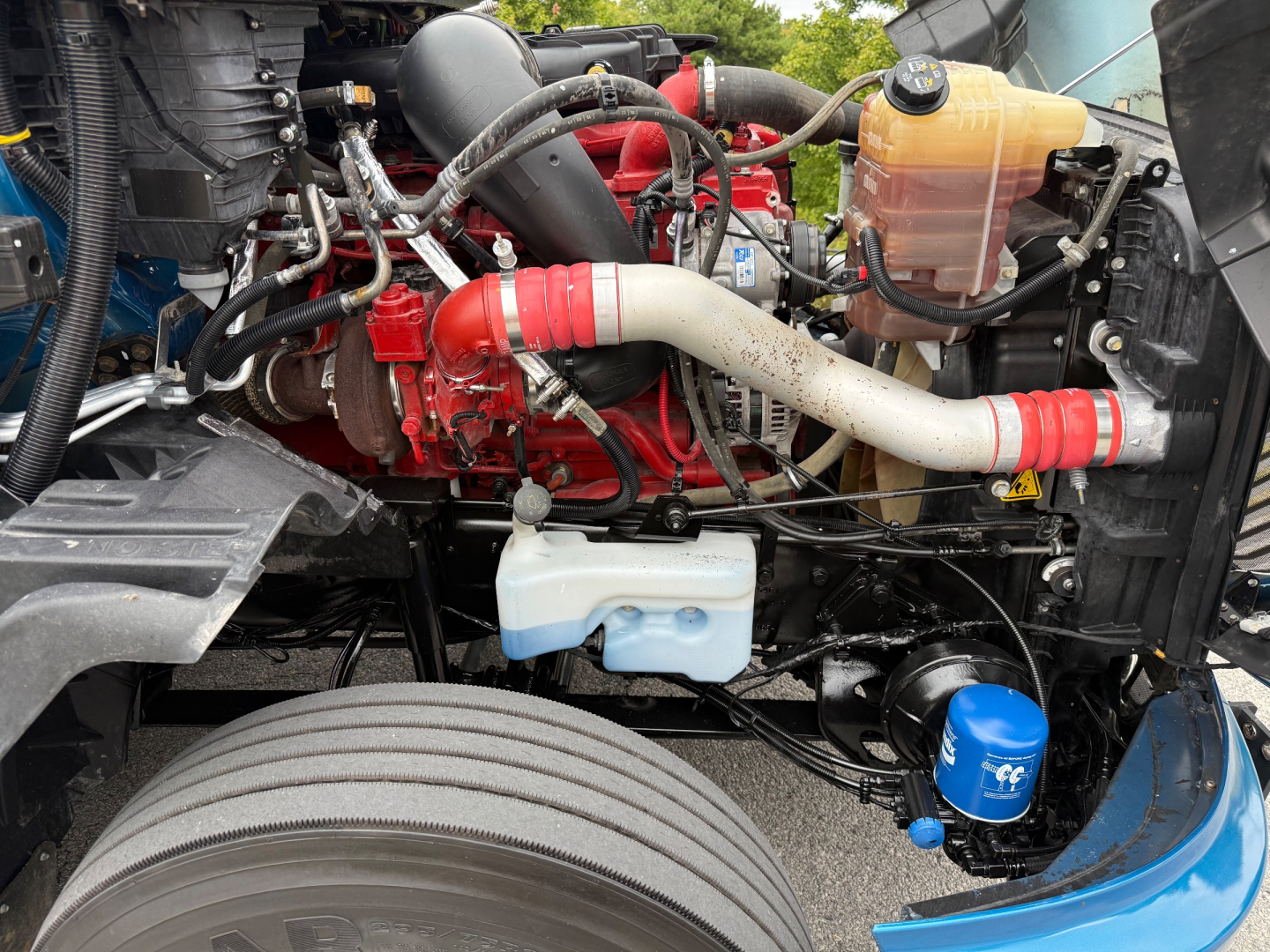 Truck engine bay with red engine, white coolant hose, blue filter, and yellow coolant reservoir visible in a 2024 International LT625 engine compartment.