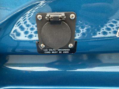 Fuel/electric inlet cover on a blue truck with label reading '110 VOLTS - GROUNDED CORD MUST BE USED'