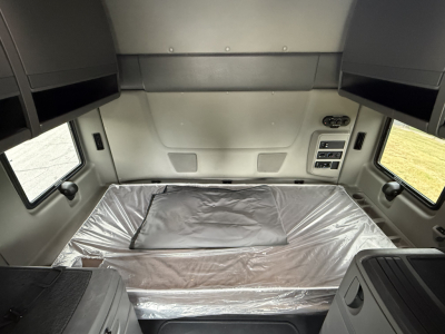 Interior cab view of a 2024 International LT625 sleeper cab showing a wrapped mattress, overhead cabinets, and control panel on the right side.