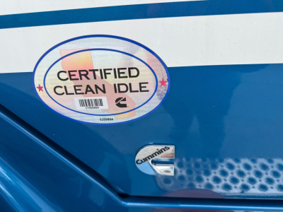 Truck rear with Certified Clean Idle badge and Cummins logo on blue surface, showing sticker and perforated metal vent area.