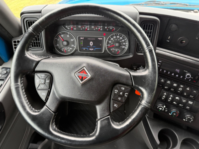 Truck cockpit showing steering wheel with International Diamond badge, instrument cluster, and dashboard controls; digital gauge display at center
