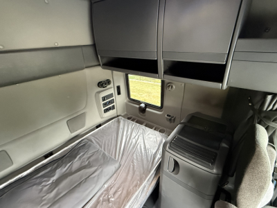 Truck sleeper cab interior showing storage cabinets, window, and a bed with plastic cover inside a used 2024 International LT625.