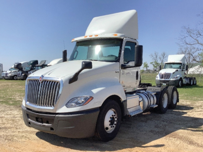 Truck engine bay area of a white 2019 International LT625 daycab shows front grille and cab with high roof; side view reveals tandem axle chassis and fuel tanks.