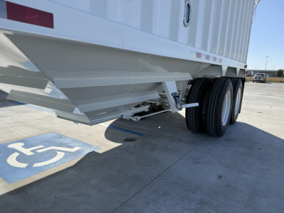 Trailer undercarriage showing steel hopper and tandem axle wheels, side of grain trailer with support beams and access ladder; handicap parking space marking in foreground.