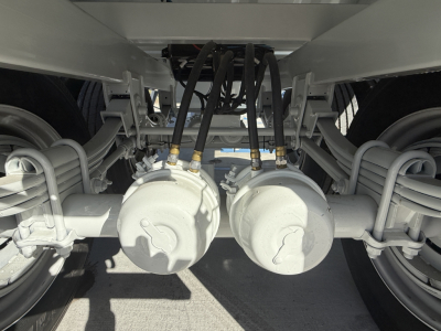 Rear view of a 2027 Armor Lite 40' steel grain hopper trailer showing dual axles, suspension, and hoses connected to landing gear and brake chambers.