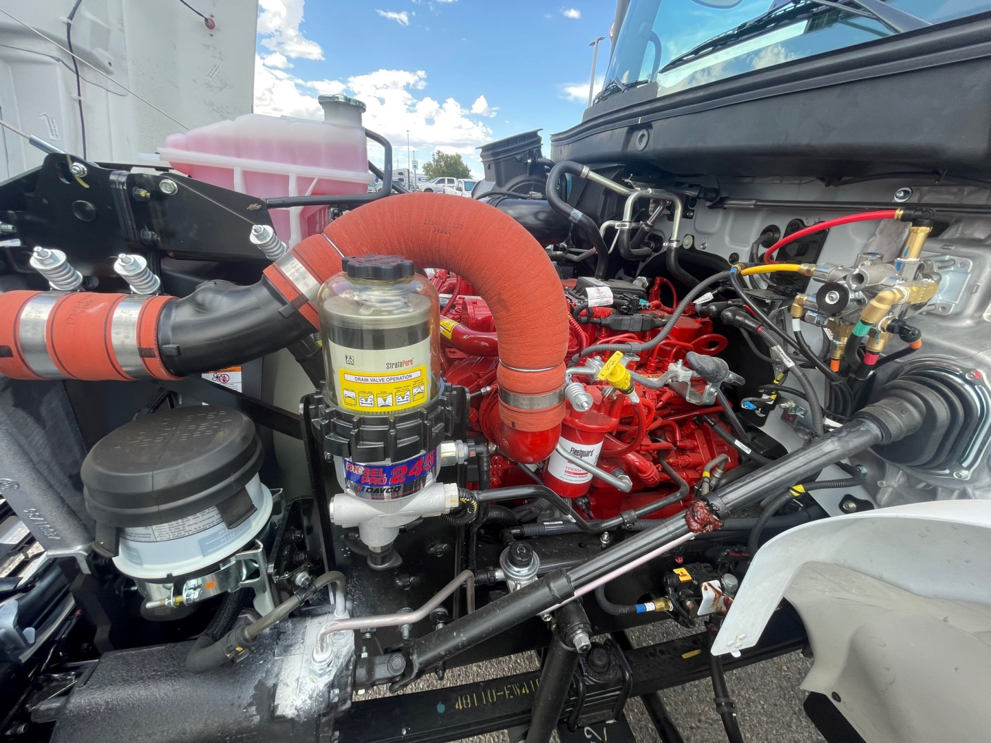 Truck engine bay showing large red turbo hoses and hydraulic lines in a new Hino L6 cab and chassis.