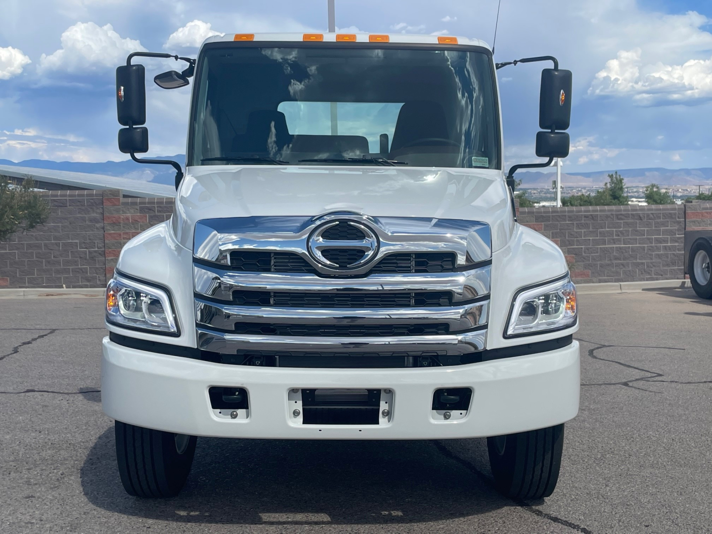 Front view of a white 2025 Hino L6 Cab and Chassis truck with chrome grille, large bumper, and dual side mirrors.